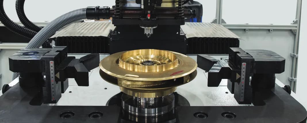 Impulsor de bomba de bronce apoyado sobre la mesa de una balanceadora vertical CIMAT, con el cabezal de corrección arriba